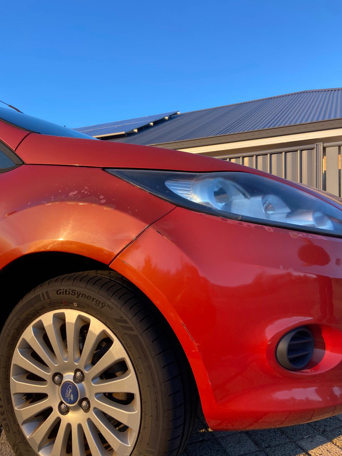 The same red Ford Fiesta front guard after treatment — the scuffing beside the headlight is gone and the panel is clean.